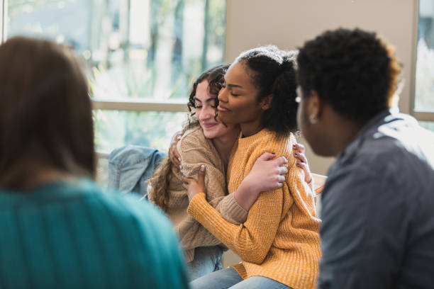 Multiracial young women hugging during emotional support group.  Mental health, therapy, friendship.